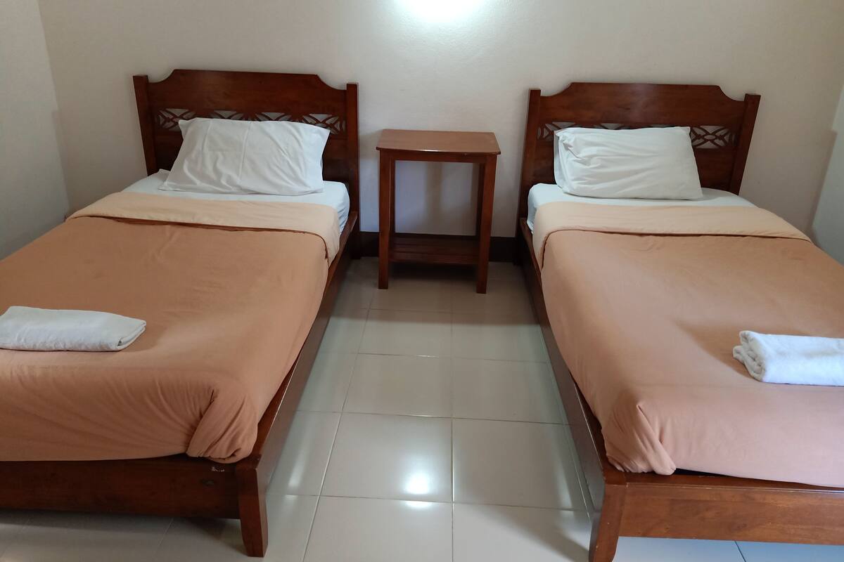 Two single beds with wooden headboards, a small wooden nightstand, and a white tiled floor.