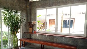 A room with a concrete wall, a wooden bench, a large window, and a potted plant. - Phumchan Place Hotel (Phayao)