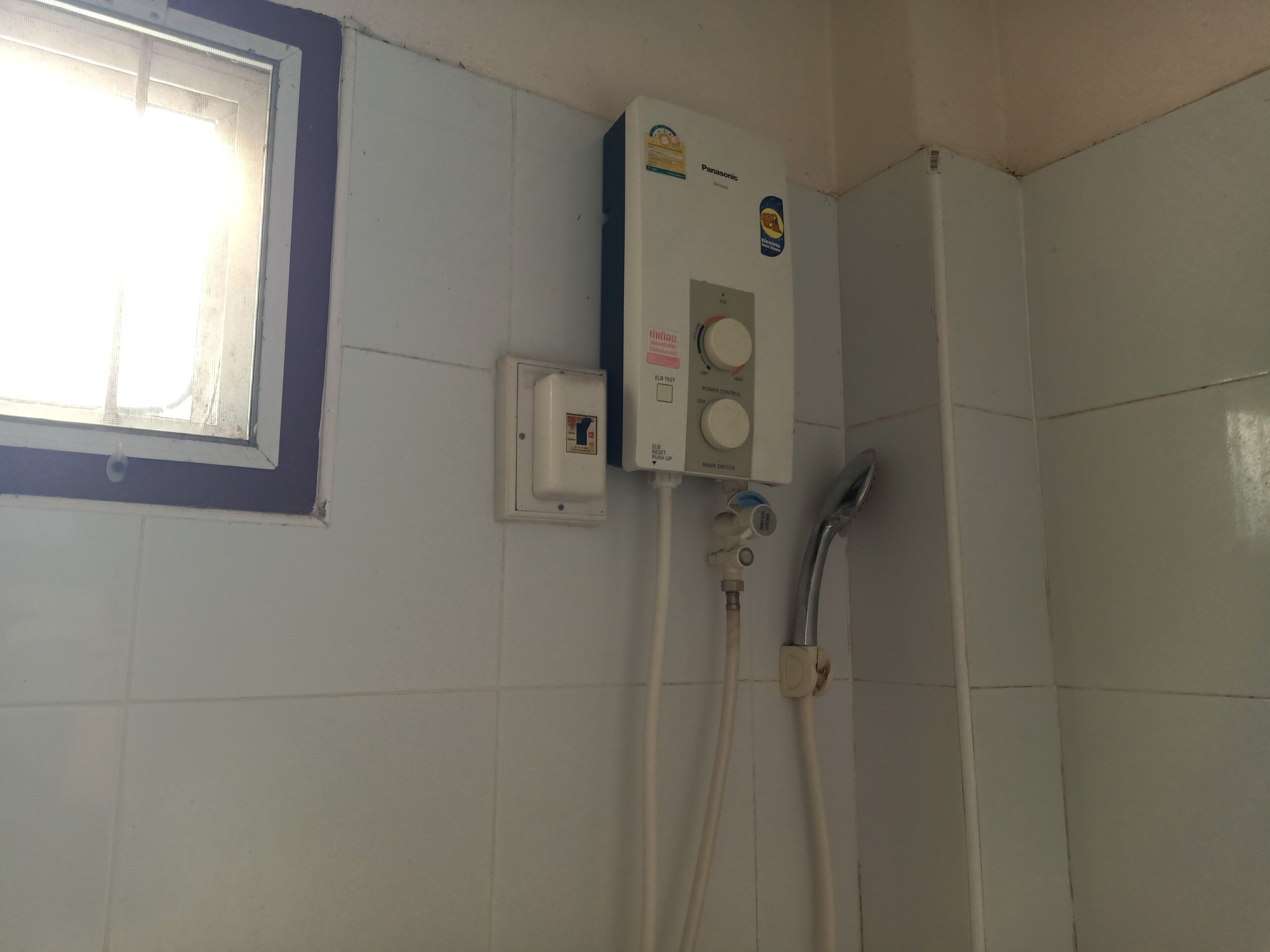A bathroom with a built-in shower, a hand dryer, and a wall-mounted electrical box.