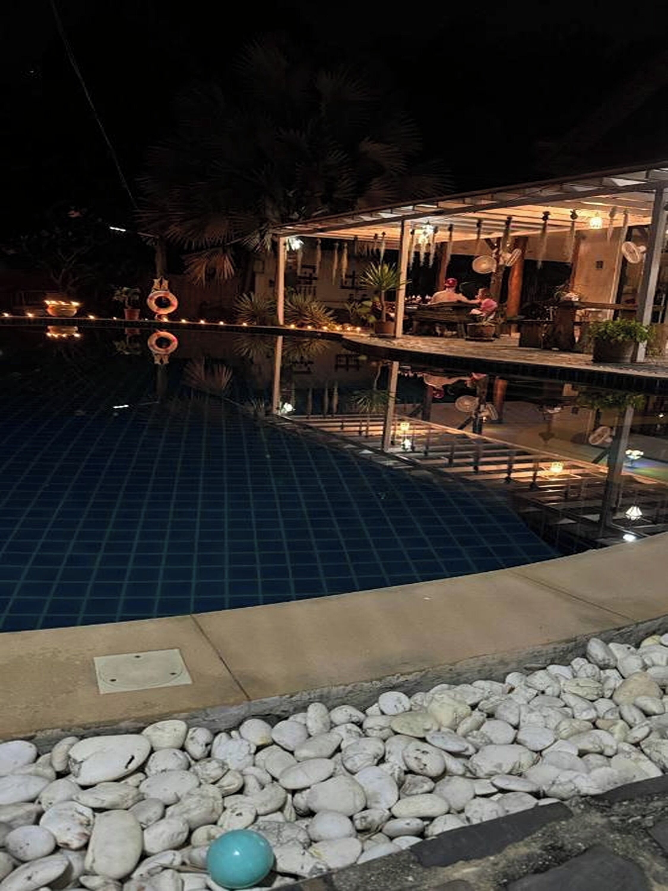 A pool area with a tiled floor, a pebble border, and a small blue object.