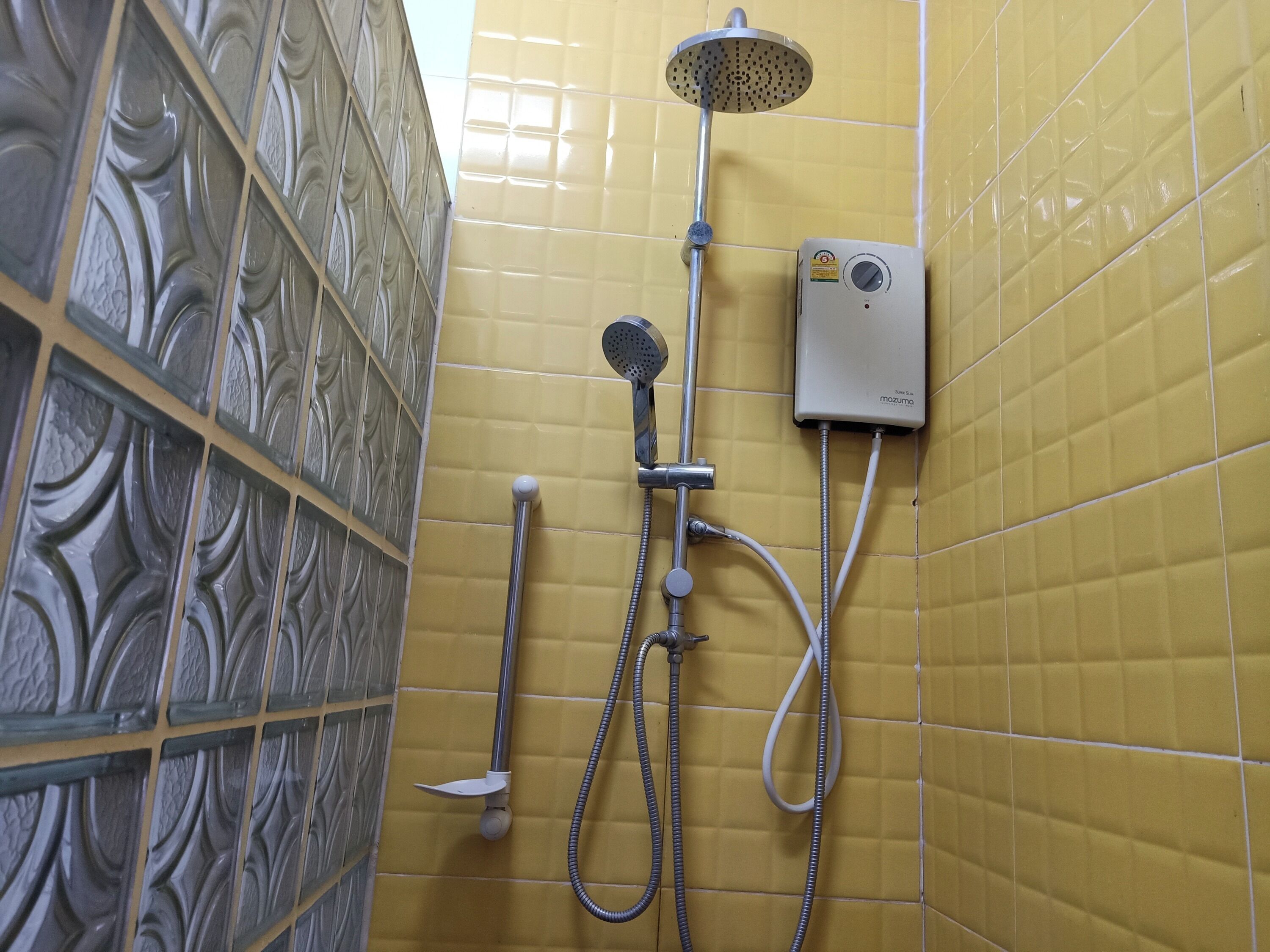 A bathroom with yellow tiled walls, a showerhead, a handheld shower, and a wall-mounted control unit.