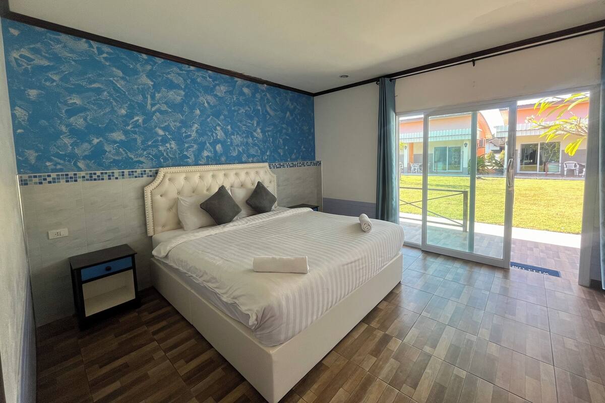 A bedroom with a large bed, a nightstand, a blue and white patterned wall, and a view of a courtyard through a sliding glass door.