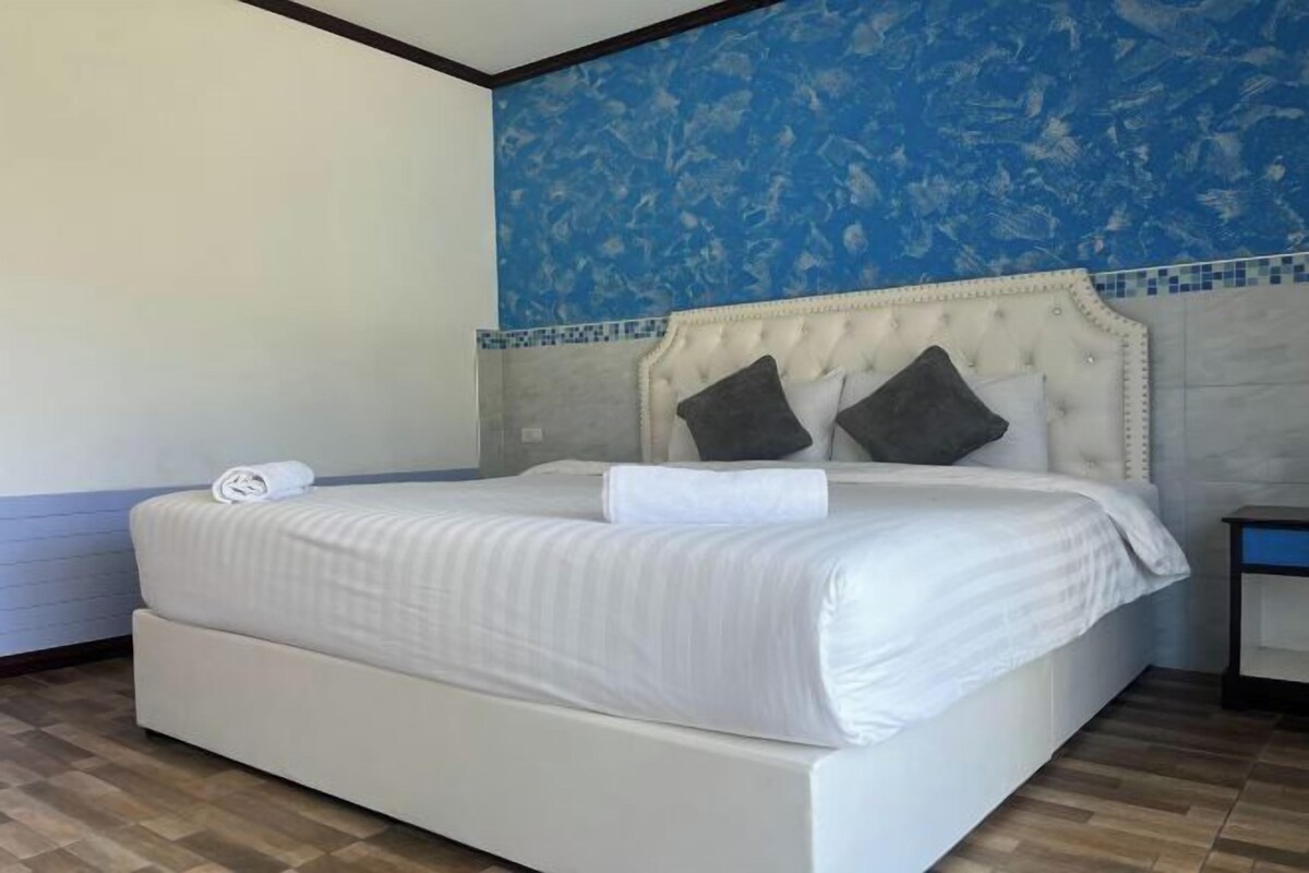 Un dormitorio con una cama grande, un cabecero con diseño capitonado y una pared azul con estampado.