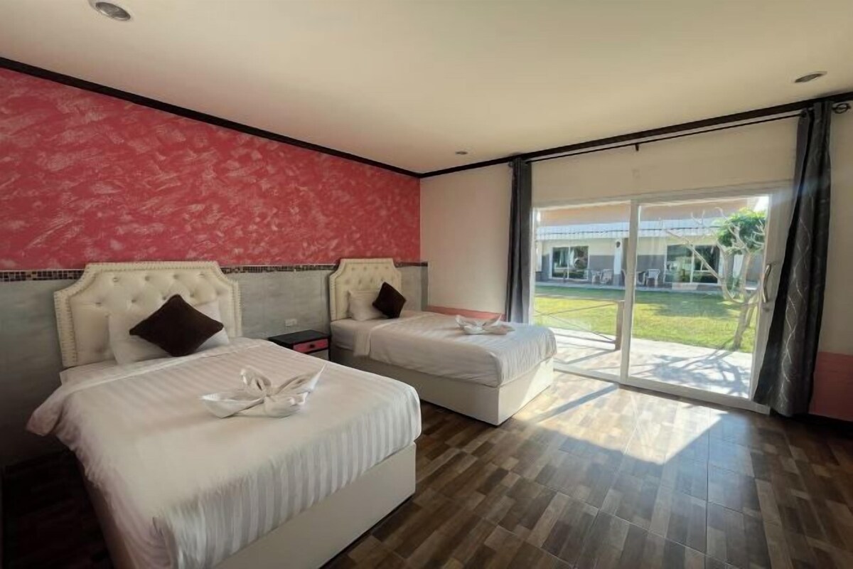 A hotel room with two beds, a red textured wall, and a large sliding glass door leading to a balcony.
