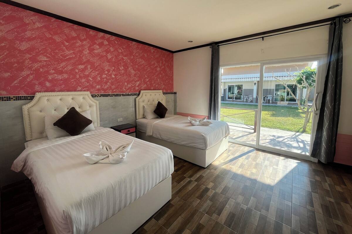 A hotel room with two beds, a red patterned wall, and a large sliding glass door leading to an outdoor area.
