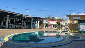 Zona de piscina con borde de azulejos, mobiliario exterior e iluminación con luces colgantes.