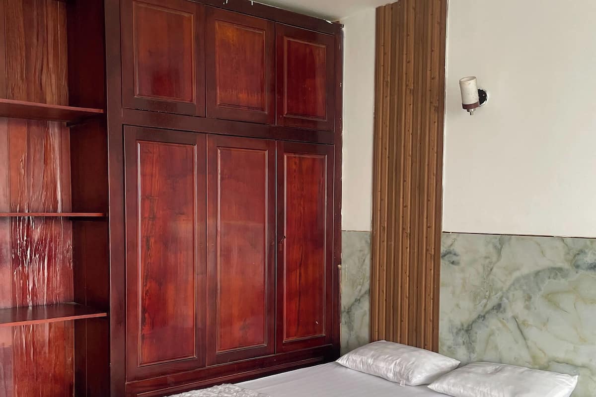 A bedroom with a large wooden wardrobe, a bed with white bedding, and a marble-patterned wall.