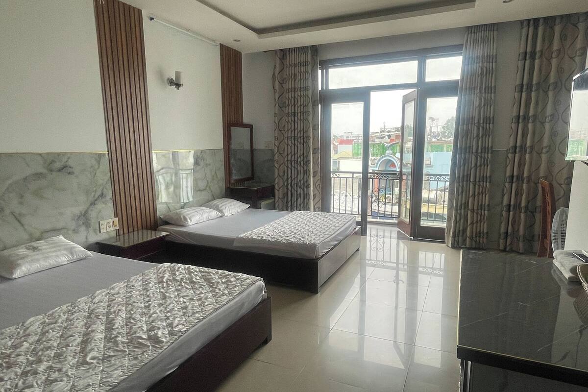 A hotel room with two beds, a marble headboard, a large window with curtains, and a balcony.