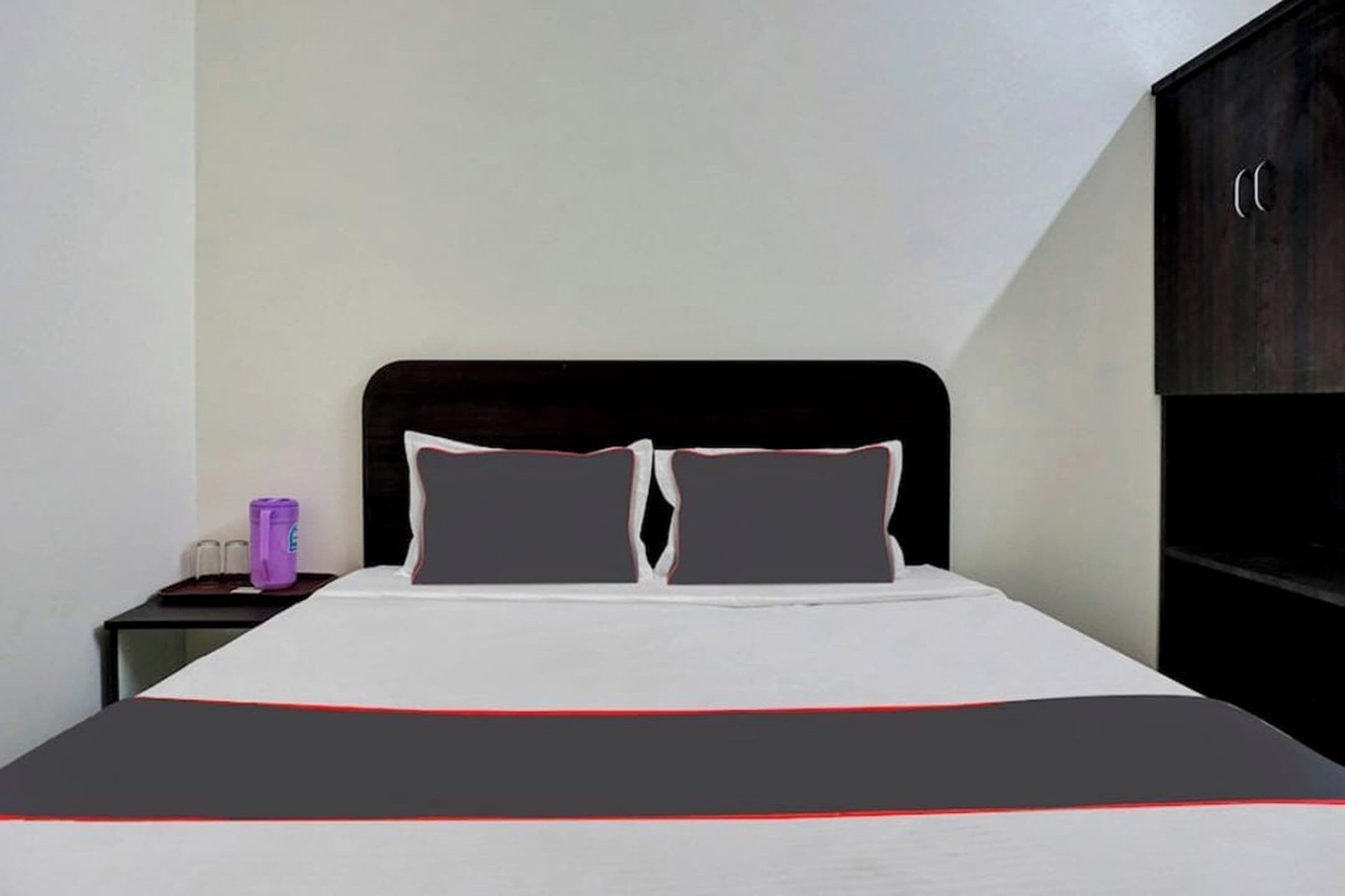 Quarto de hotel com cama, mesa de cabeceira, armário de madeira escura e parede branca.