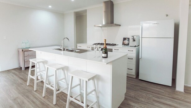 Een moderne keuken met een centraal eiland, witte kasten, een roestvrijstalen afzuigkap, een ingebouwde oven en een koelkast.