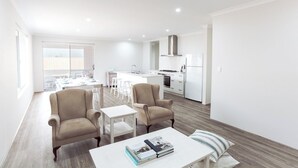 Een modern appartement met een eethoek, twee fauteuils, een kleine salontafel en een keuken met witte apparatuur.