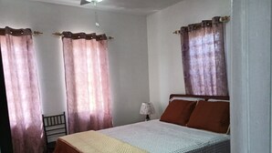 A bedroom with a bed, curtains, a chair, and a ceiling fan.