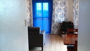 A room with a ceiling fan, a sofa, a wooden dining table with chairs, and patterned curtains.
