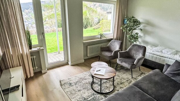 A modern living room with a grey sofa, two armchairs, a coffee table, and a view of a green landscape through large windows. - Rothaarsteig by Interhome (Winterberg)