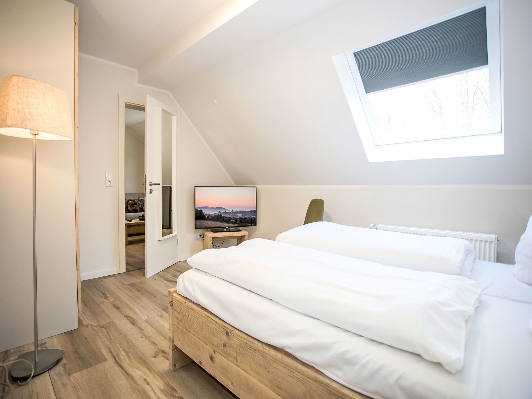 Une chambre avec un plafond en pente, un téléviseur posé sur une petite table et une vue sur l’extérieur par une fenêtre.
