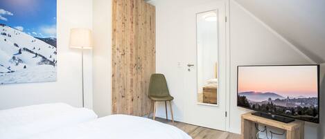 Una habitación de hotel moderna con una cama grande, un armario de madera, una silla, un televisor y un cuadro de un paisaje nevado.