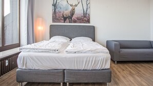 A modern bedroom with a large bed, grey upholstered bench, and a deer painting on the wall. - Fernblick by Interhome (Winterberg)