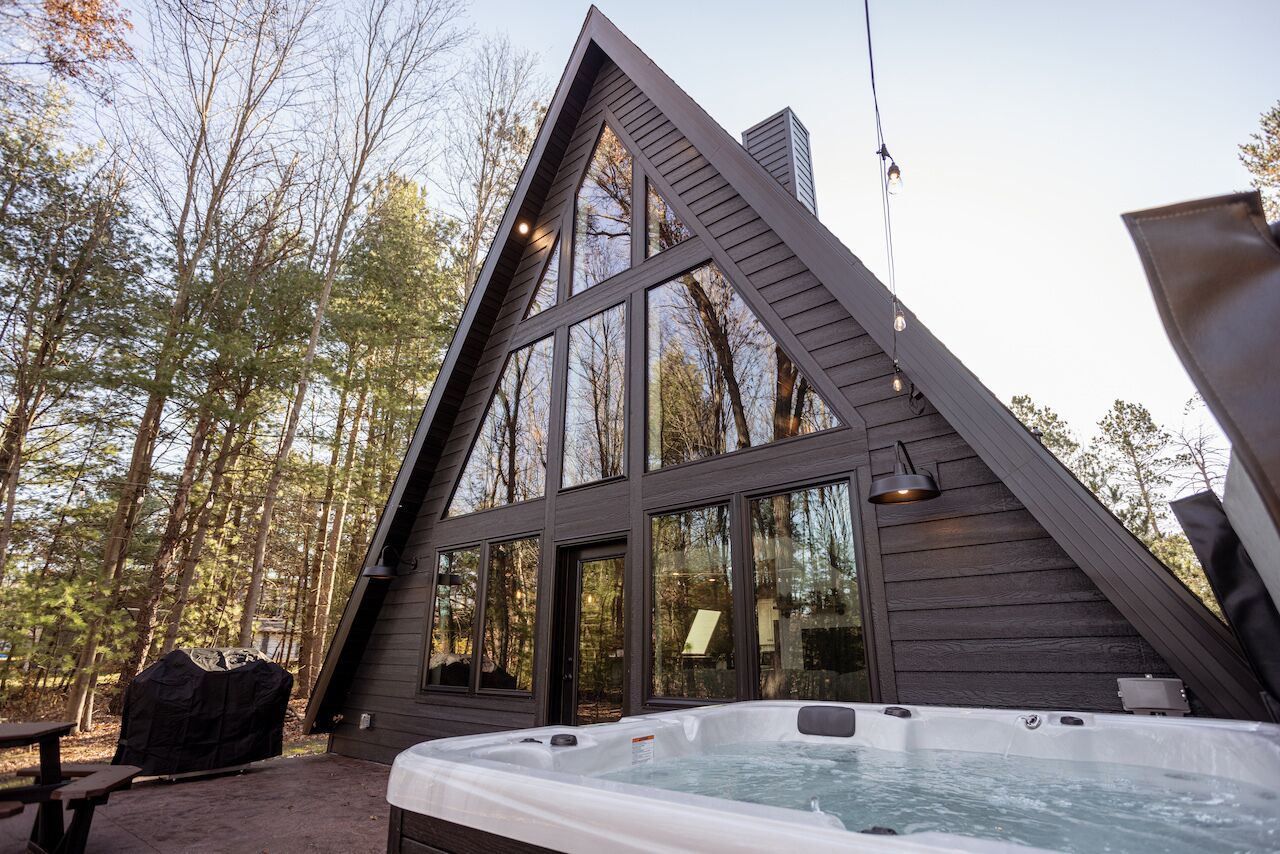 Una cabaña con jacuzzi, ventanas amplias y una mesa de picnic.