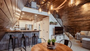 A modern kitchen with a bar area, a dining table with chairs, and a staircase leading to an upper level. - HOT TUB and gorgeous lake views-The Lily Pad A Frame-minutes from Dells (Wisconsin Dells)