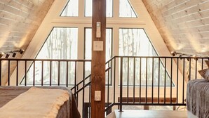 A bedroom with a sloped ceiling, wooden beams, a large window, and a bed with a headboard. - HOT TUB and gorgeous lake views-The Lily Pad A Frame-minutes from Dells (Wisconsin Dells)