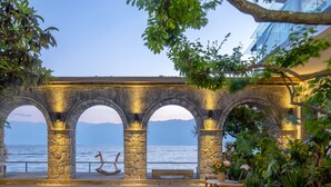 A stone archway with a bench and table, overlooking a body of water with mountains in the background. - Dali Lanting Seaview Resort Hotel (Dali)