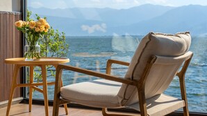 A wooden chair with a cushion and a small table with a vase of flowers, positioned by a window overlooking a body of water and mountains. - Dali Lanting Seaview Resort Hotel (Dali)