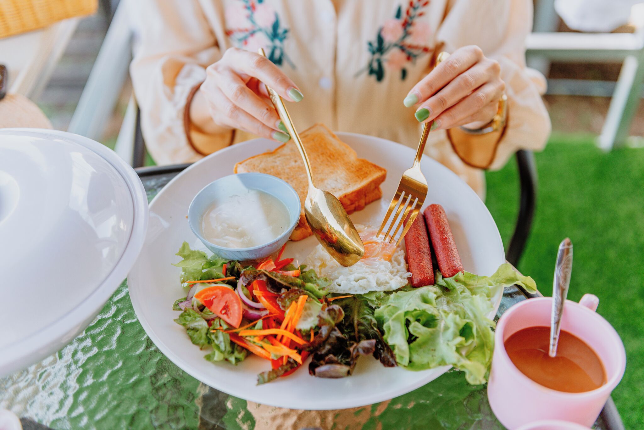 A plate with a salad, rice, and two sausages, a bowl of soup, and a pink cup with a spoon.