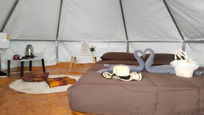 Una tienda de campaña con una cama, almohadas, una mesita con una tetera y una cisne decorativa.