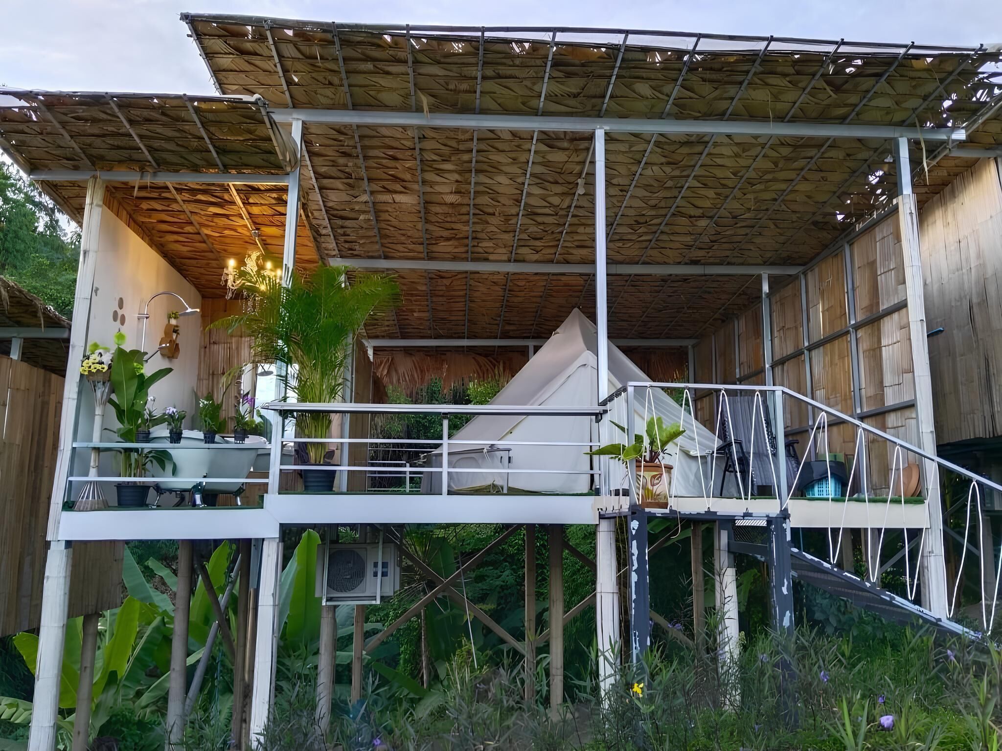 Une structure moderne à plusieurs niveaux, dotée d’un toit de chaume, d’un espace extérieur aménagé et d’une végétation luxuriante.