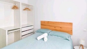 Makuuhuone, jossa on sänky, puinen pääty, valkoinen vaatekaappi ja pieni yöpöytä.