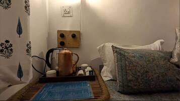 Una habitación acogedora con cama, una mesita de centro con un libro, un hervidor y un enchufe de pared.