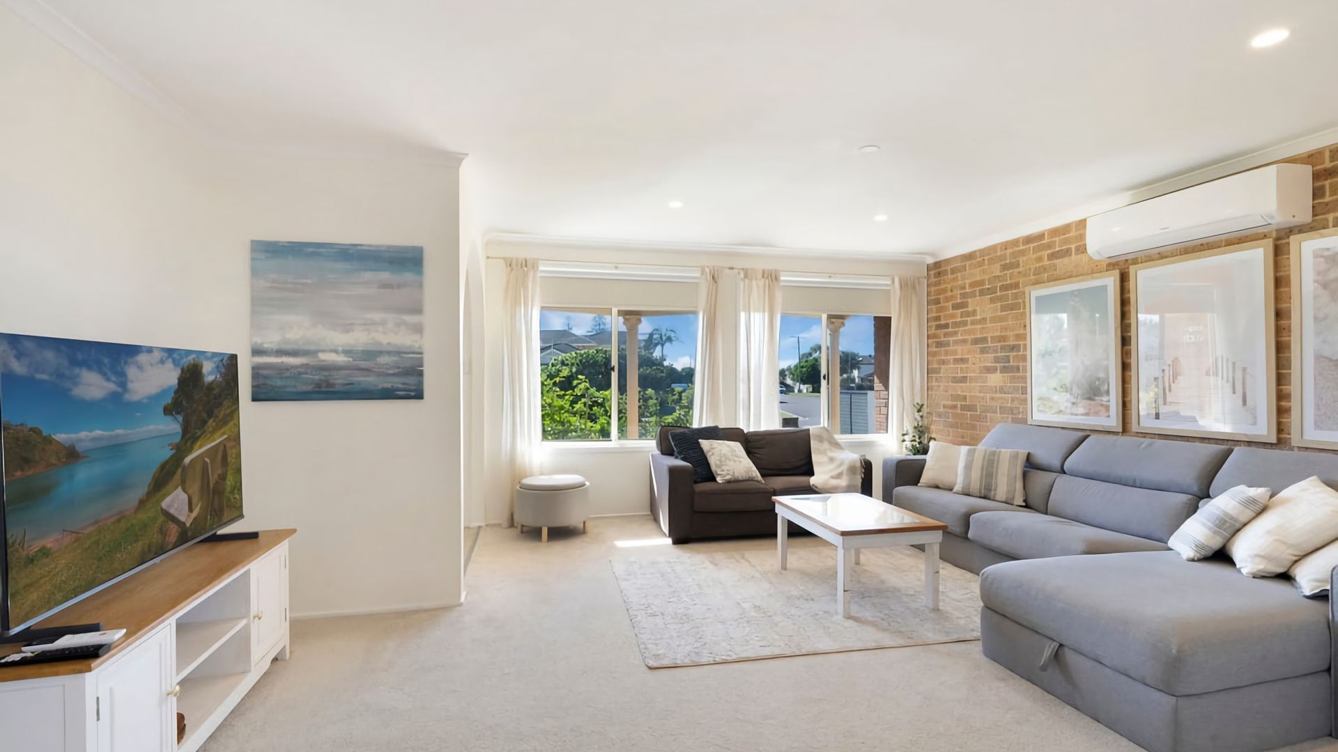 A modern living room with a large grey sofa, a coffee table, a TV on a wooden stand, and artwork on the walls.