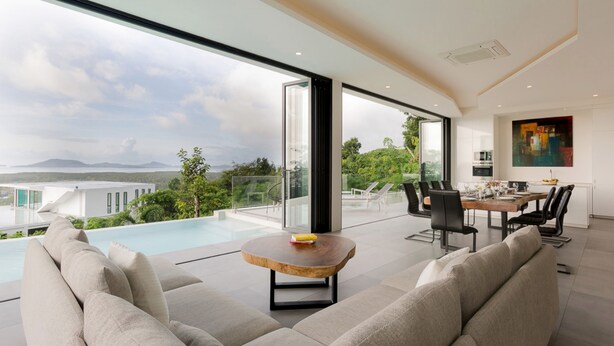 A modern living room with a pool, large windows, and a dining area. - Yamu Hills Panoramic Ocean View 6 Bed Luxury Vila (Pa Klok)