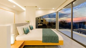 A modern bedroom with a large bed, a nightstand, and a view of the cityscape through large windows. - Yamu Hills Panoramic Ocean View 6 Bed Luxury Vila (Pa Klok)