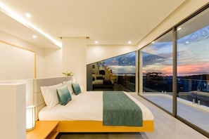 Un dormitorio moderno con una cama grande, una mesita de noche y vistas a la ciudad a través de amplios ventanales.