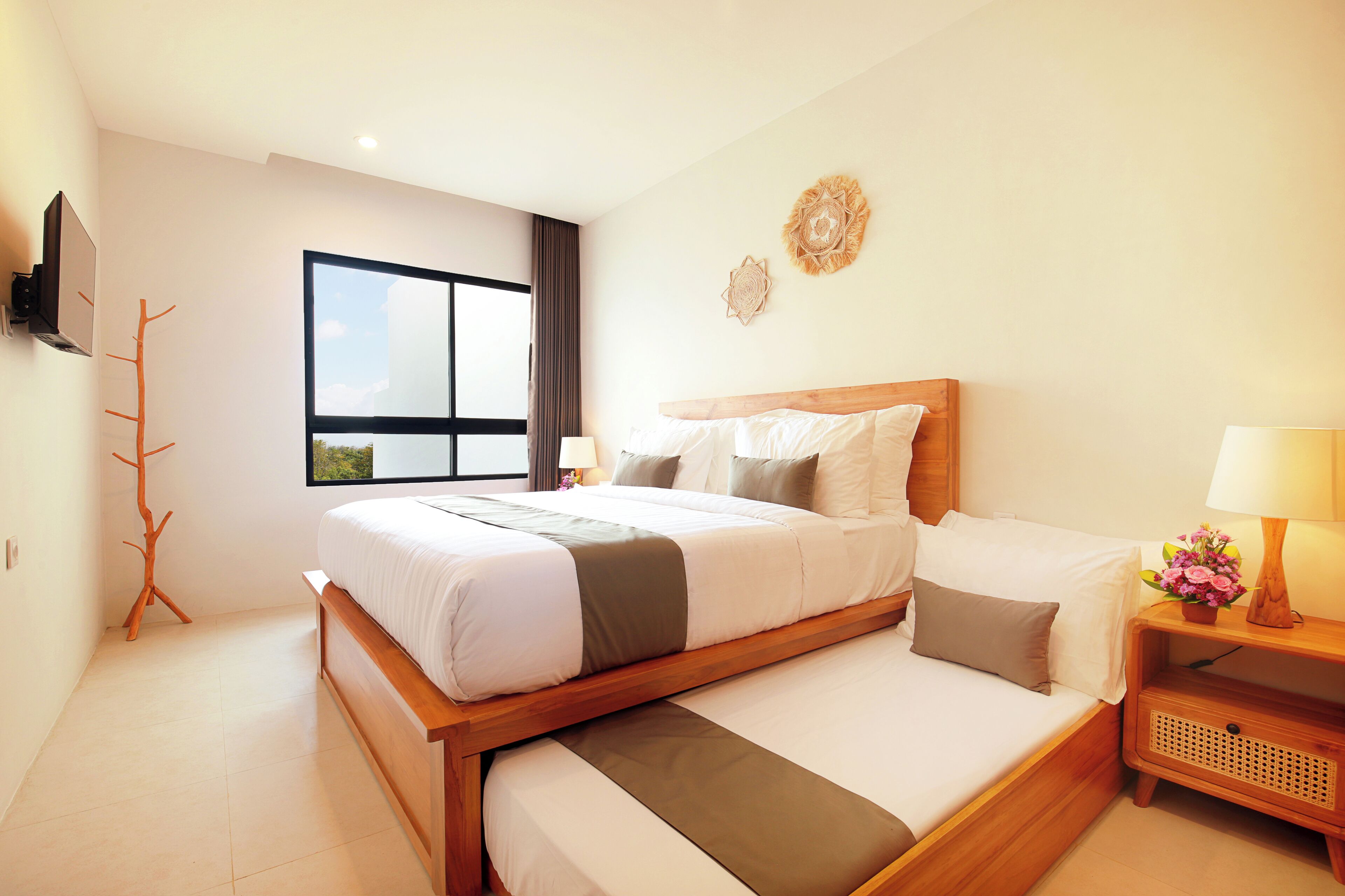 A modern hotel room with a large bed, a TV mounted on the wall, and a window with a view of the sky.