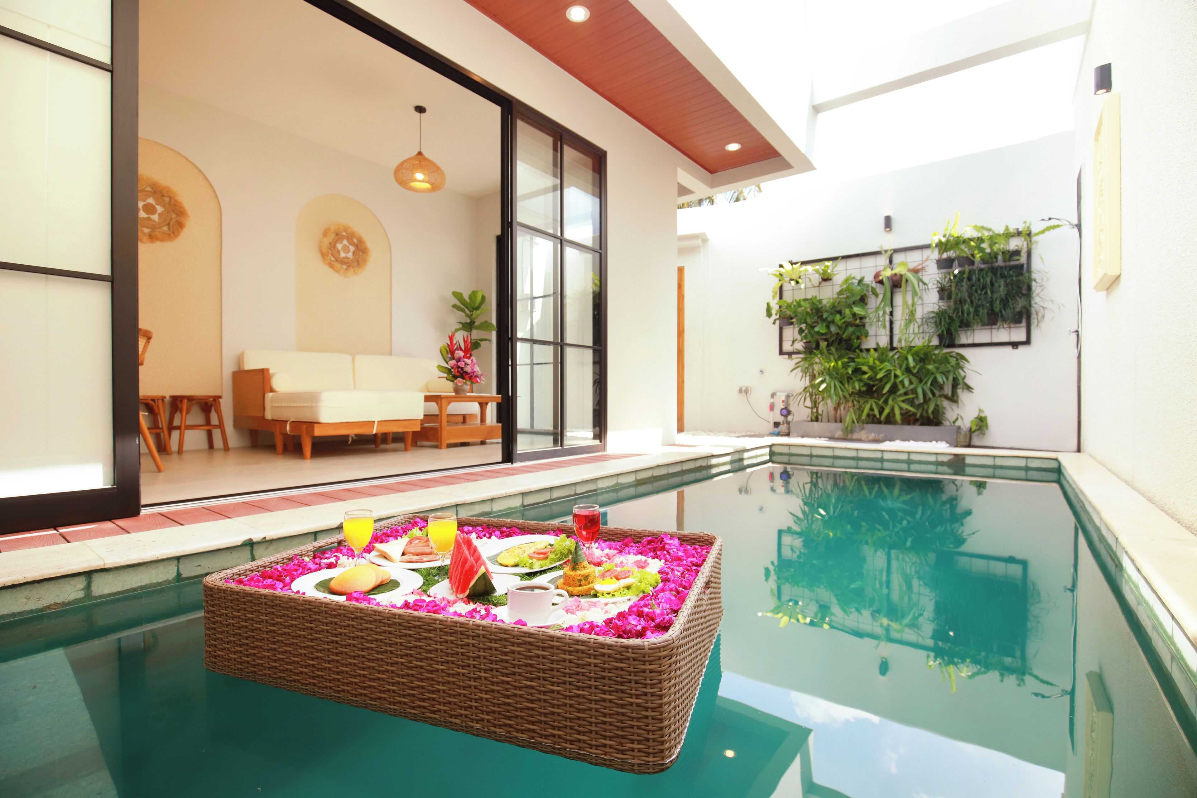 A poolside dining area with a wicker table set with food and drinks, surrounded by a pool.