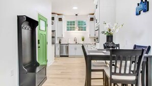 A modern kitchen with white cabinets, a green door, and a dining area with a table and chairs. - Entire home, in Goldsboro North Carolina (Goldsboro)