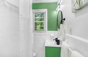 A bathroom with white tiles, a green accent wall, a window, a towel rack, and a mirror. - Entire home, in Goldsboro North Carolina (Goldsboro)