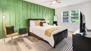 A modern bedroom with a green accent wall, a bed with a black headboard, a bedside table, a chair, a TV, and a window with a view of greenery. - Entire home, in Goldsboro North Carolina (Goldsboro)