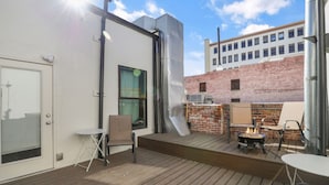 A rooftop patio with a grill, seating, and a view of a brick building.