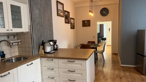Ett modernt kök med vita skåp, en bänkskiva i trä och en kaffebryggare. På väggen hänger inramade tavlor och det finns en klocka.