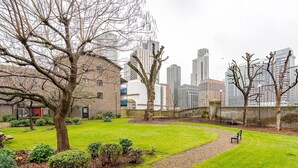 A courtyard with a grassy area, trees, and a brick building. - London - Apartment - Riverside - Sleeps 3 - Garden (London)