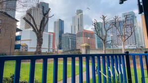 A cityscape with modern high-rise buildings, a grassy area, and a blue railing. - London - Apartment - Riverside - Sleeps 3 - Garden (London)