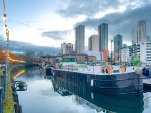 A river with a boat docked, surrounded by tall buildings and a cloudy sky.