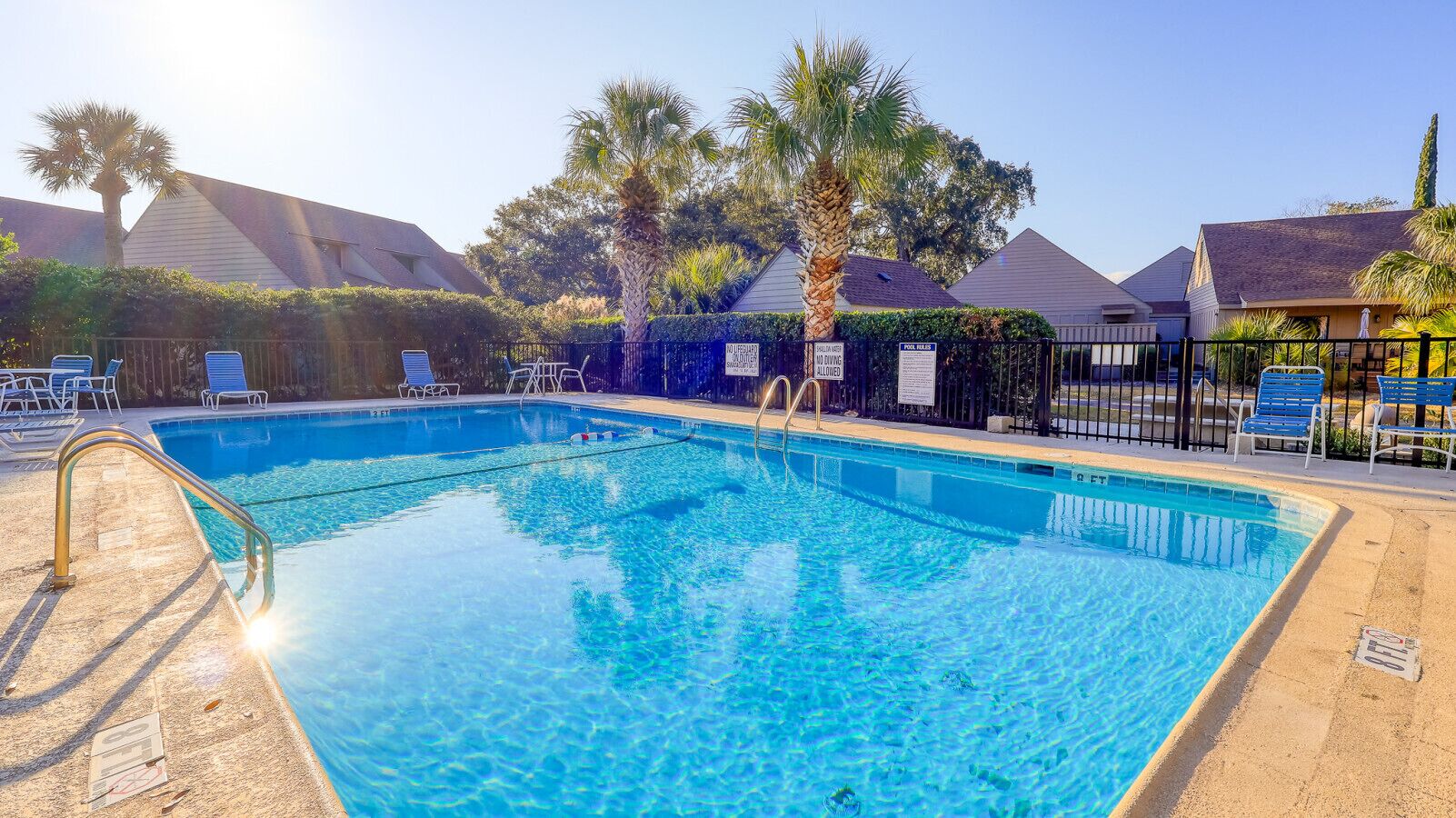 A clear blue swimming pool with a metal ladder, surrounded by lounge chairs and palm trees.