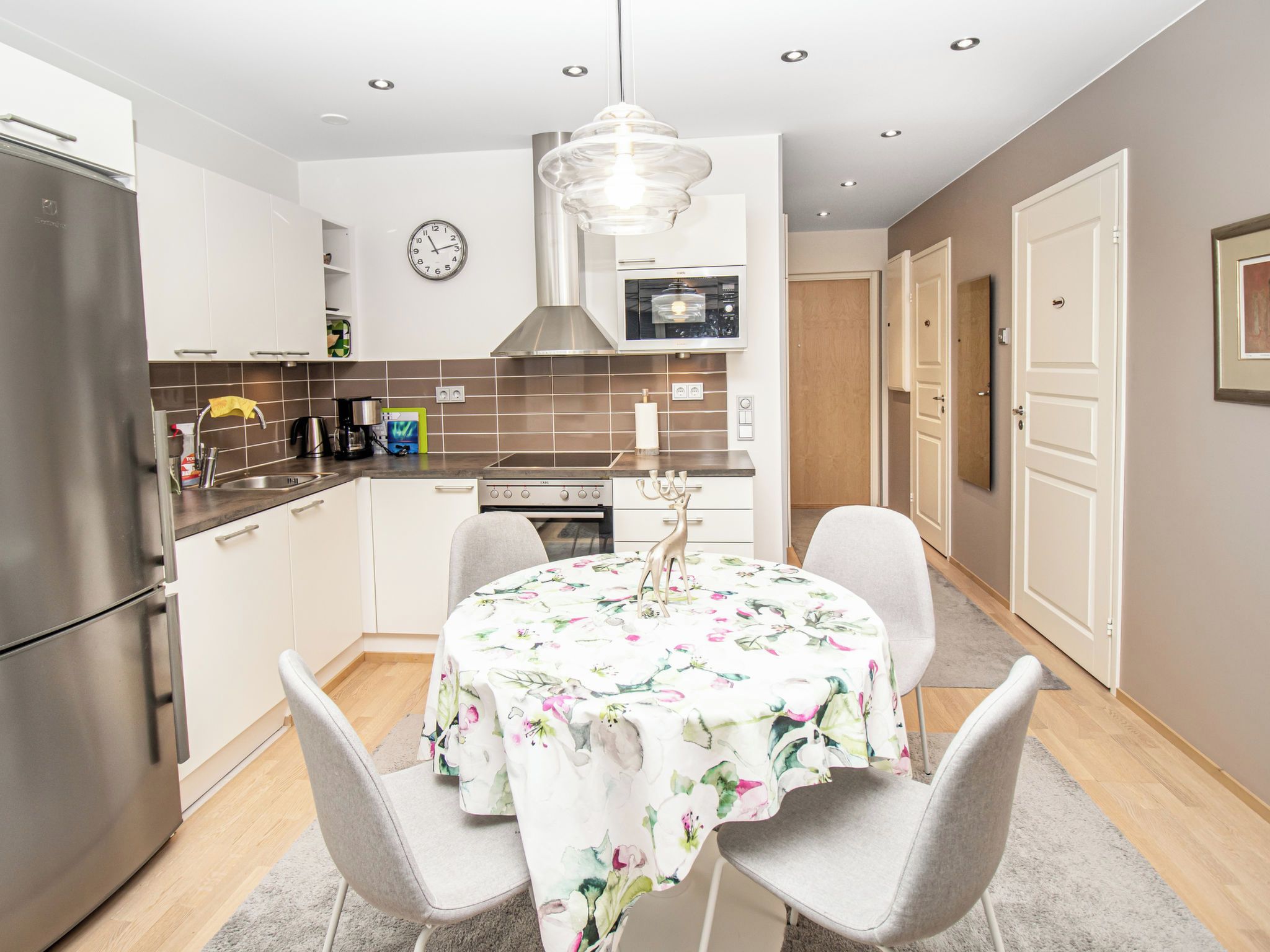 Een moderne keuken met een eettafel, stoelen en een klok aan de muur.