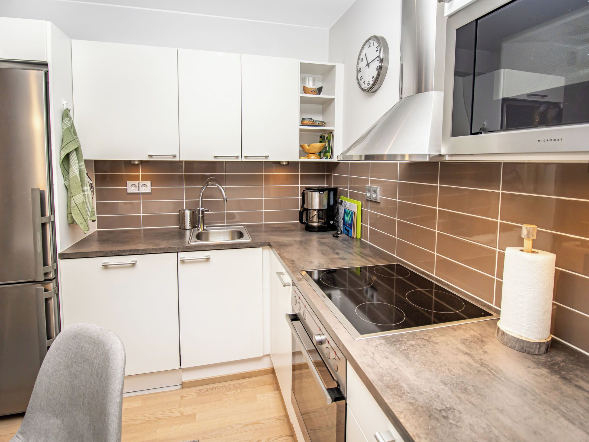 Une cuisine moderne avec des meubles blancs, un réfrigérateur en acier inoxydable, un four à micro-ondes et une plaque de cuisson à induction noire.