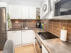 Une cuisine moderne avec des meubles blancs, un réfrigérateur en acier inoxydable, un four à micro-ondes et une plaque de cuisson à induction noire.