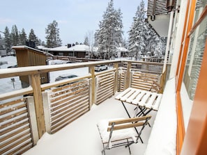 A balcony with wooden railings, a white cushioned bench, and a view of snow-covered trees and buildings. - Kelotähti a 11 by Interhome (Inari)